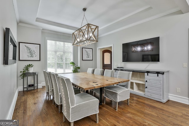 dining room with arched walkways, wood finished floors, a raised ceiling, a notable chandelier, and ornamental molding