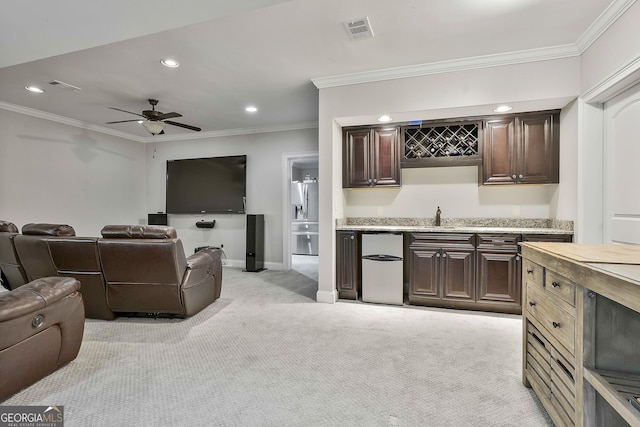 living area with light carpet, indoor wet bar, a ceiling fan, visible vents, and ornamental molding