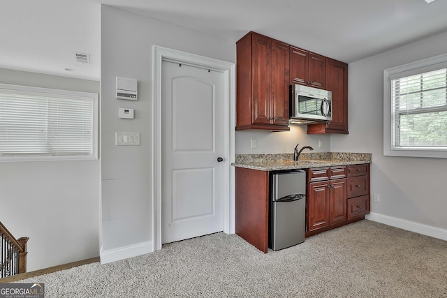 kitchen featuring light stone countertops, light colored carpet, freestanding refrigerator, stainless steel microwave, and visible vents