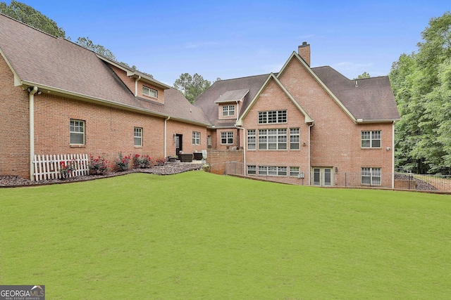 back of property featuring a lawn, brick siding, fence, and a chimney
