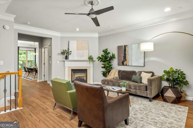 living room featuring a ceiling fan, crown molding, a fireplace, light wood-type flooring, and baseboards