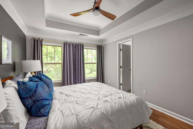 bedroom featuring visible vents, ornamental molding, wood finished floors, baseboards, and a tray ceiling