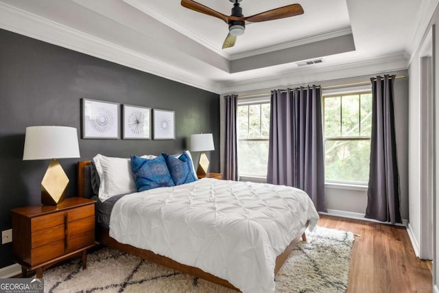 bedroom featuring a raised ceiling, baseboards, wood finished floors, visible vents, and ornamental molding