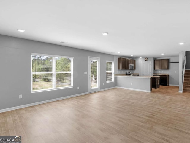 unfurnished living room with light wood-style floors, baseboards, recessed lighting, and stairs