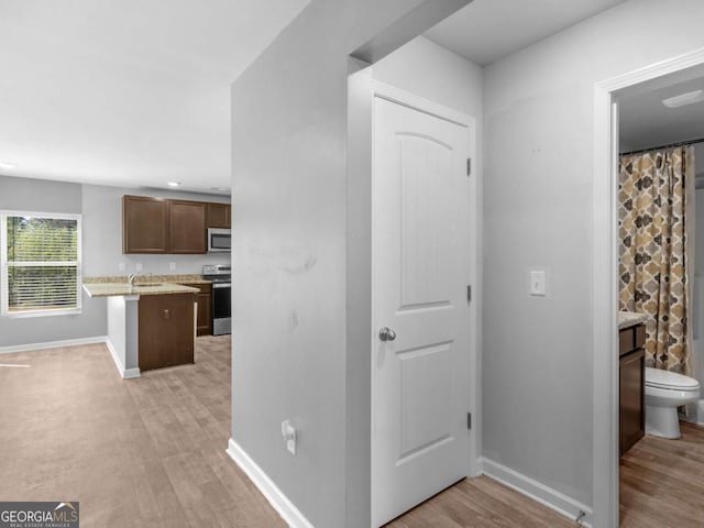hall featuring baseboards, a sink, and light wood-style floors