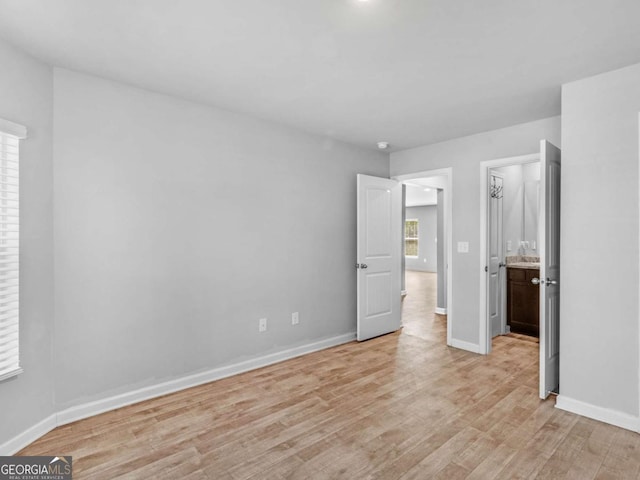 unfurnished bedroom with baseboards, ensuite bathroom, and light wood-type flooring