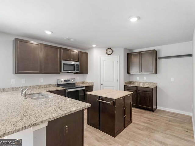 kitchen featuring appliances with stainless steel finishes, dark brown cabinets, a sink, baseboards, and light wood-style flooring