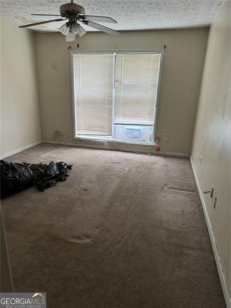 empty room with carpet flooring, a textured ceiling, baseboards, and a ceiling fan