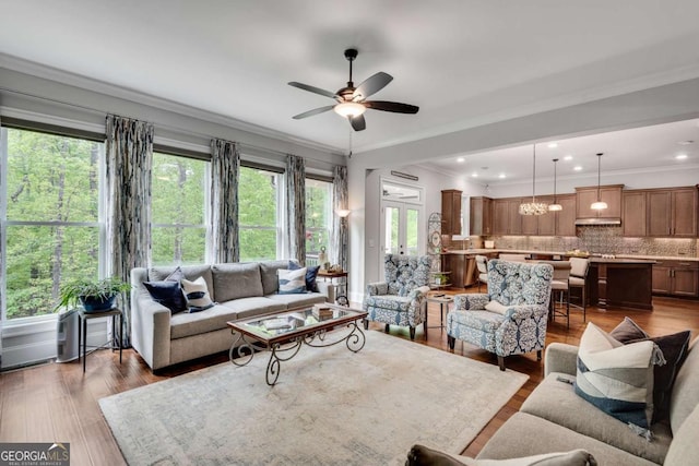 living room featuring ceiling fan, wood finished floors, ornamental molding, and a chandelier