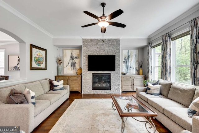 living room featuring ceiling fan, arched walkways, dark wood-type flooring, a fireplace, and crown molding