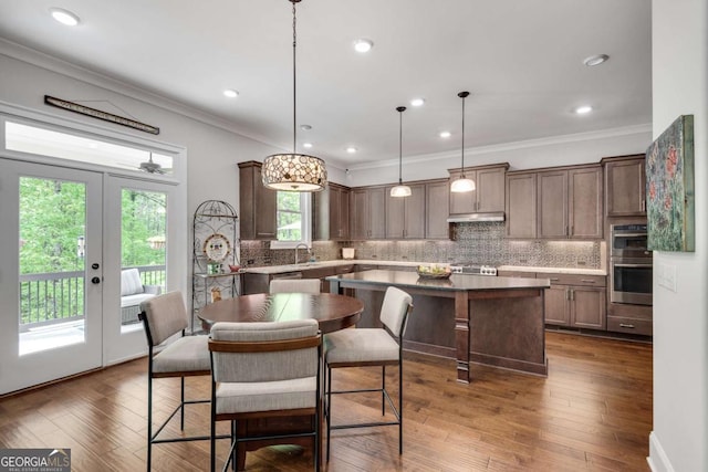 kitchen featuring ornamental molding, under cabinet range hood, tasteful backsplash, a kitchen island, and stainless steel double oven