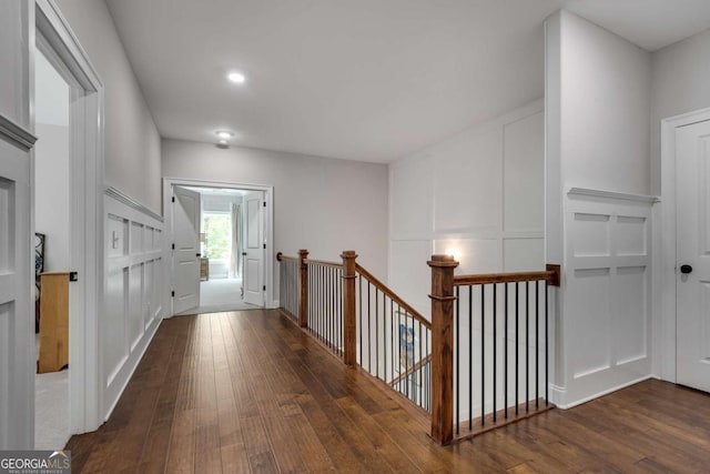 hallway with an upstairs landing, hardwood / wood-style flooring, and a decorative wall
