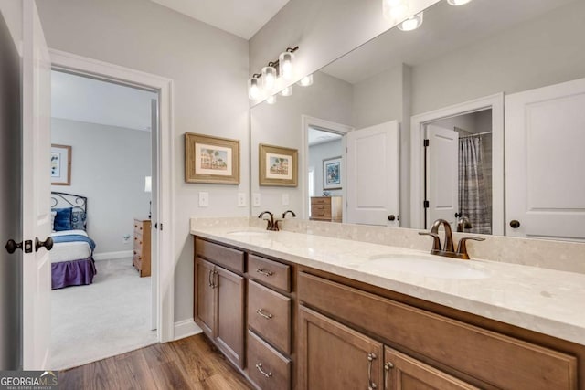 ensuite bathroom with wood finished floors, double vanity, and baseboards