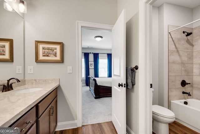ensuite bathroom featuring wood finished floors, vanity, toilet, baseboards, and tub / shower combination