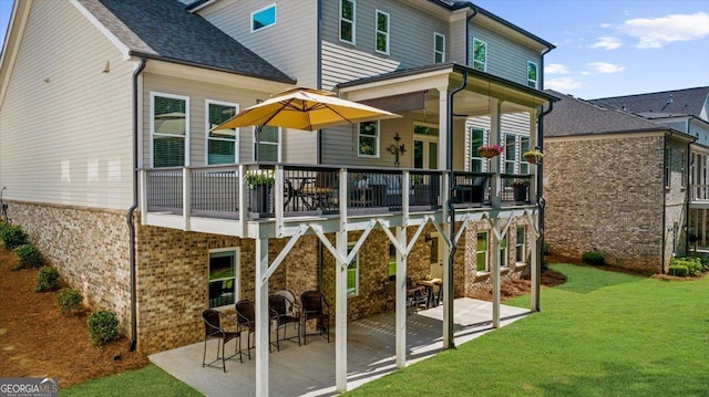 rear view of property with a yard, brick siding, a patio area, a wooden deck, and a shingled roof
