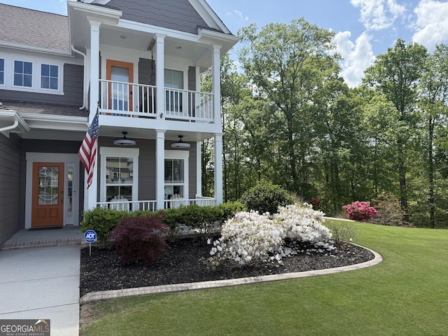view of side of property featuring covered porch, a lawn, a balcony, and roof with shingles