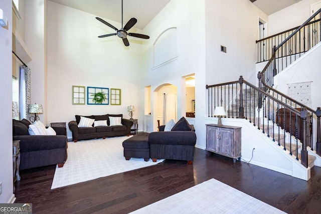 living room with arched walkways, ceiling fan, wood finished floors, and a high ceiling