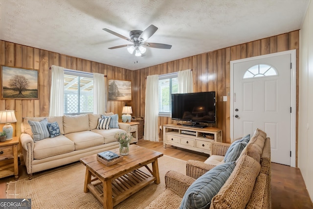 living area with wood walls, ceiling fan, light wood-type flooring, and a textured ceiling