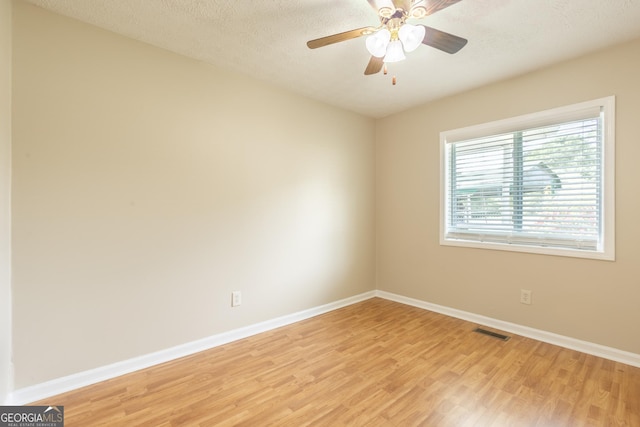 unfurnished room with a textured ceiling, a ceiling fan, baseboards, light wood-type flooring, and visible vents