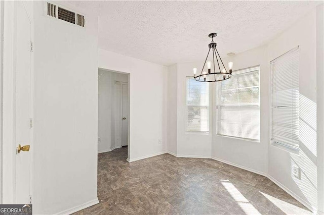 unfurnished dining area featuring visible vents, a textured ceiling, baseboards, and a chandelier