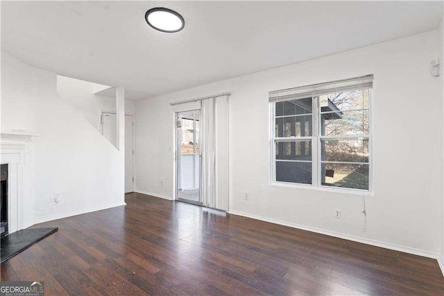 unfurnished living room featuring baseboards, a fireplace with raised hearth, and wood finished floors