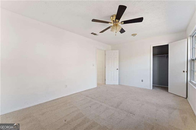 unfurnished bedroom with ceiling fan, a textured ceiling, carpet, visible vents, and a closet