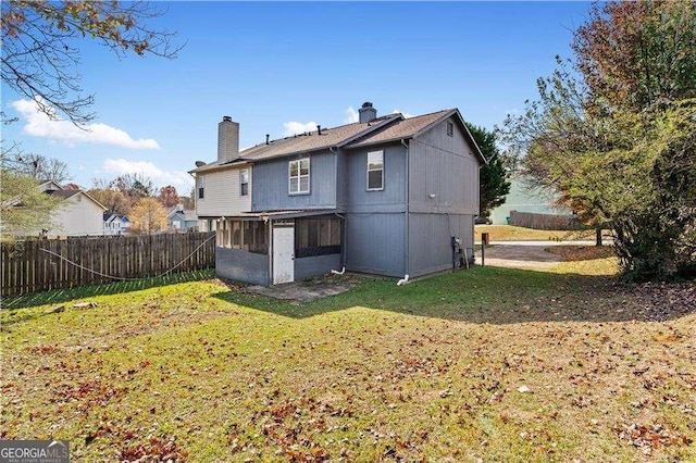 back of property featuring a lawn, a chimney, a fenced backyard, and a sunroom