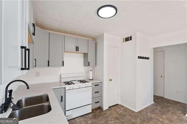 kitchen featuring visible vents, white range with gas stovetop, gray cabinets, a textured ceiling, and a sink