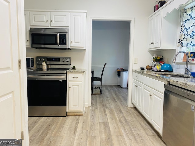 kitchen featuring light stone countertops, light wood-type flooring, white cabinets, a sink, and appliances with stainless steel finishes