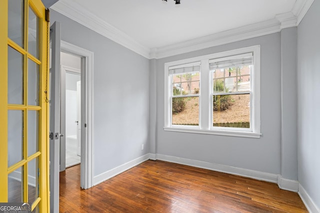 spare room featuring crown molding, baseboards, and dark wood finished floors