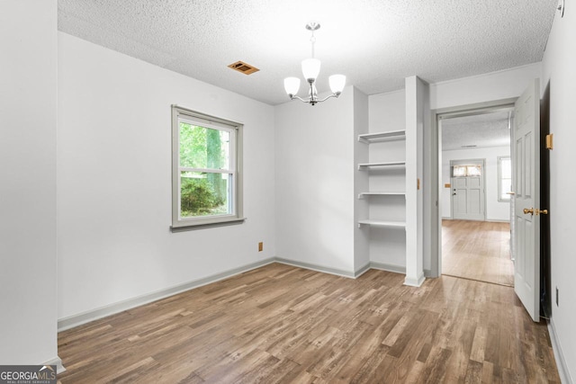 unfurnished bedroom with wood finished floors, a textured ceiling, baseboards, visible vents, and a notable chandelier