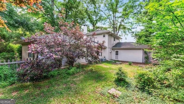 back of house featuring a chimney, central AC, fence, and a lawn