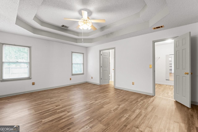 unfurnished bedroom featuring a textured ceiling, visible vents, wood finished floors, and a raised ceiling