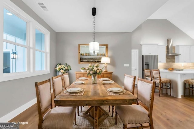 dining space with baseboards, visible vents, lofted ceiling, and light wood-type flooring
