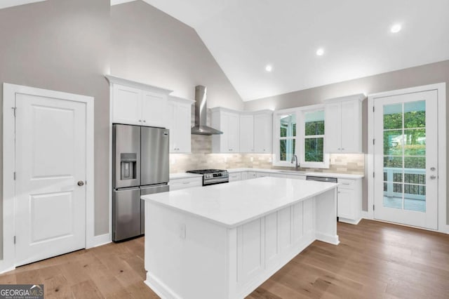 kitchen with wall chimney range hood, appliances with stainless steel finishes, white cabinets, and a kitchen island