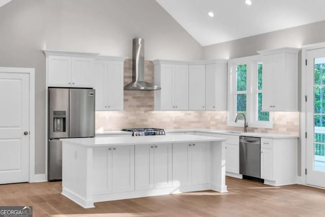 kitchen featuring wall chimney range hood, white cabinetry, appliances with stainless steel finishes, and a kitchen island