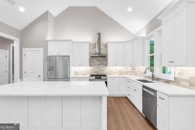 kitchen featuring wall chimney range hood, appliances with stainless steel finishes, a sink, and white cabinetry