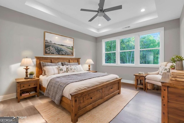 bedroom featuring light wood-style floors, baseboards, a tray ceiling, and visible vents