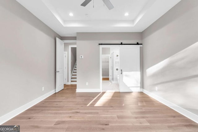unfurnished bedroom featuring baseboards, a barn door, a raised ceiling, and wood finished floors