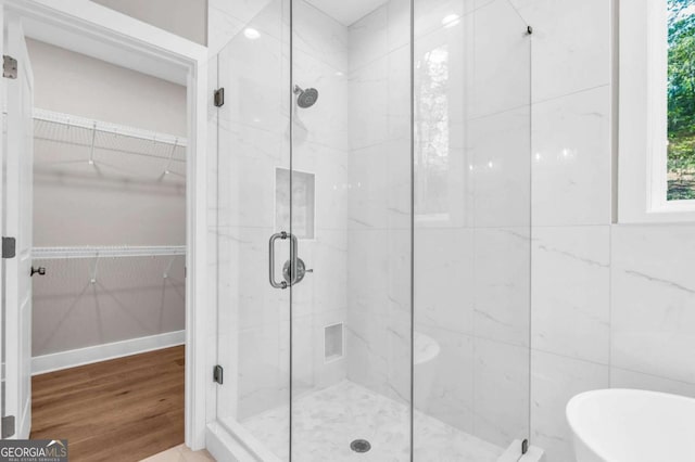 bathroom with a marble finish shower, wood finished floors, a spacious closet, and a soaking tub