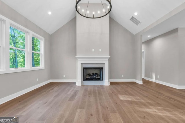 unfurnished living room featuring a notable chandelier, a fireplace, high vaulted ceiling, wood finished floors, and visible vents