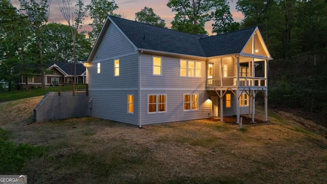 back of property at dusk featuring a shingled roof