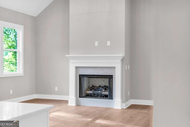 unfurnished living room with baseboards, lofted ceiling, wood finished floors, and a fireplace