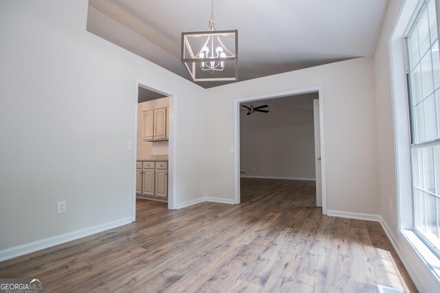 unfurnished dining area with a healthy amount of sunlight, baseboards, wood finished floors, and a chandelier