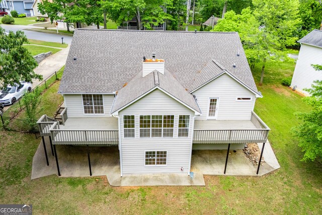 back of property featuring roof with shingles, a wooden deck, a chimney, a patio, and a yard
