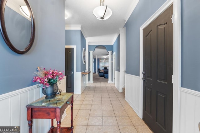 hall featuring a decorative wall, arched walkways, a wainscoted wall, decorative columns, and light tile patterned floors