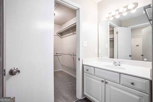 full bath featuring vanity, baseboards, a textured ceiling, and a spacious closet