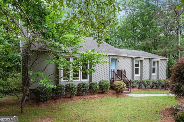 ranch-style house featuring a shingled roof and a front yard