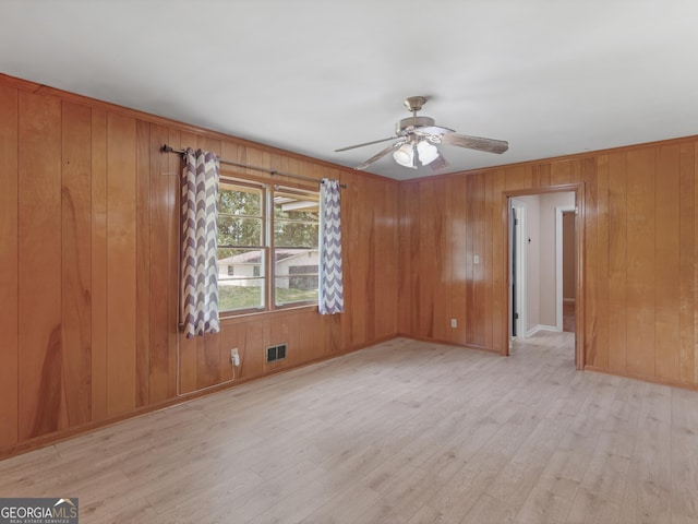 spare room featuring visible vents, wood walls, wood finished floors, baseboards, and a ceiling fan