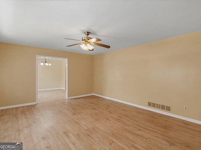 empty room with visible vents, light wood-style floors, ceiling fan with notable chandelier, and baseboards